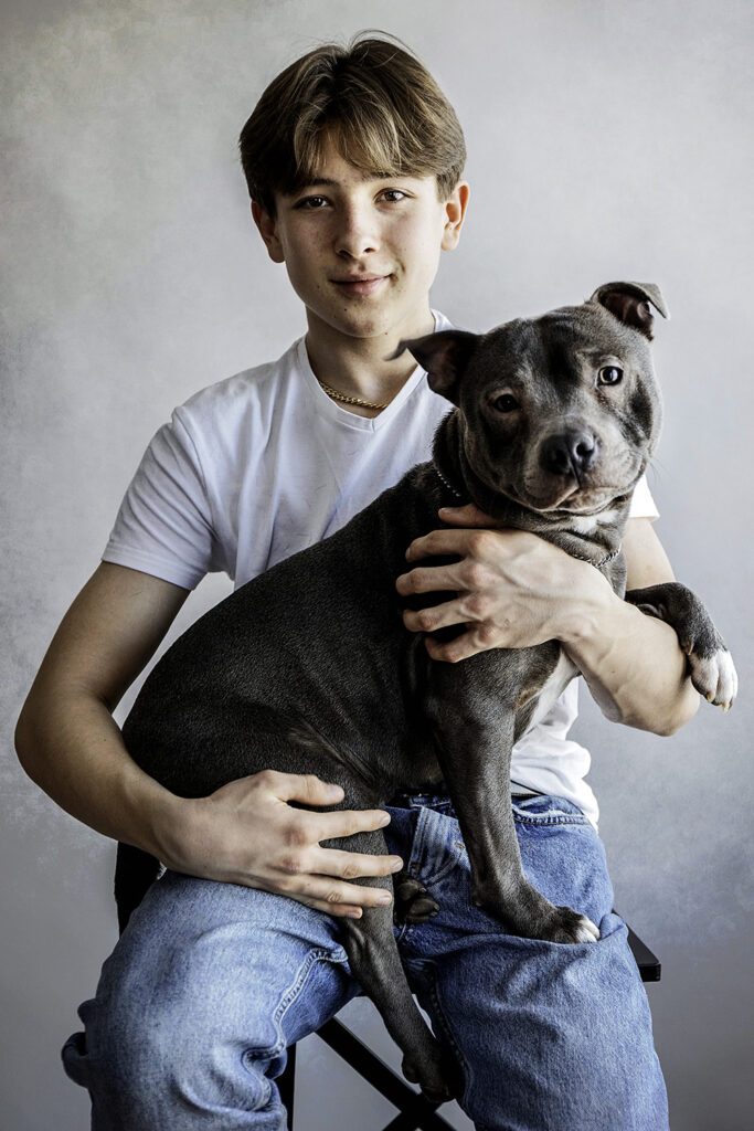 tenåringsgutt i hvit t-skjorte og blå jeans som holder en hund i armene